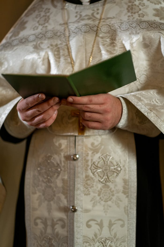Priest in traditional vestment holding a religious book during a ceremony indoors.