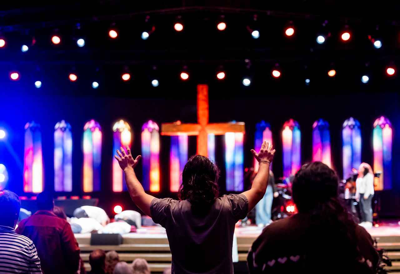 About Lively church service with congregation worshipping under colorful stained-glass lighting.