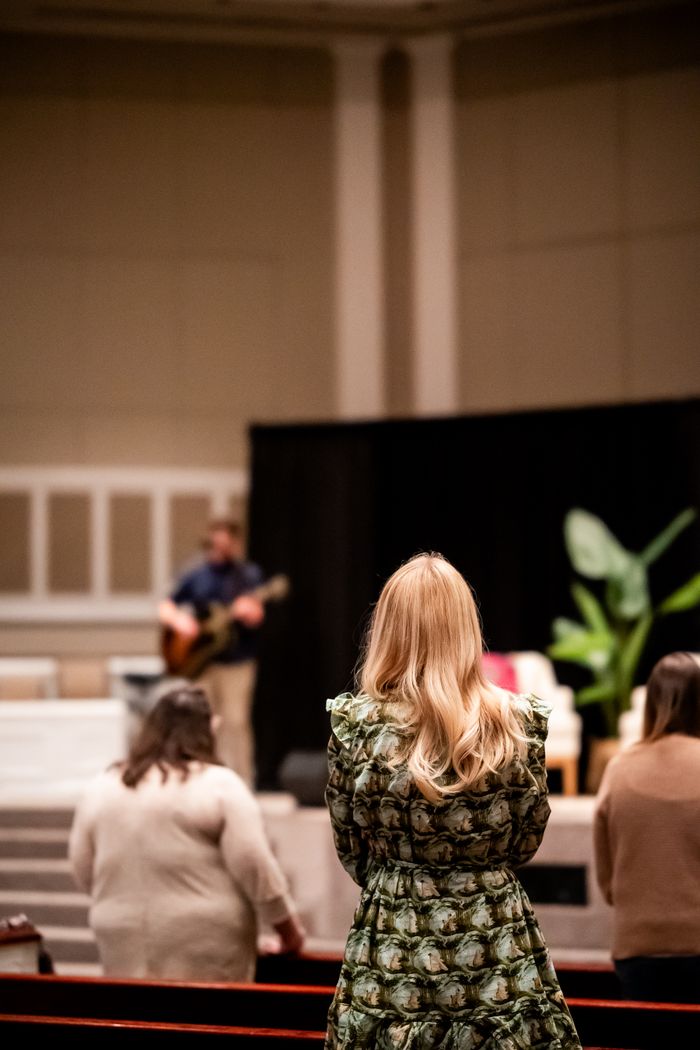 A church service with people worshiping and a musician on stage.